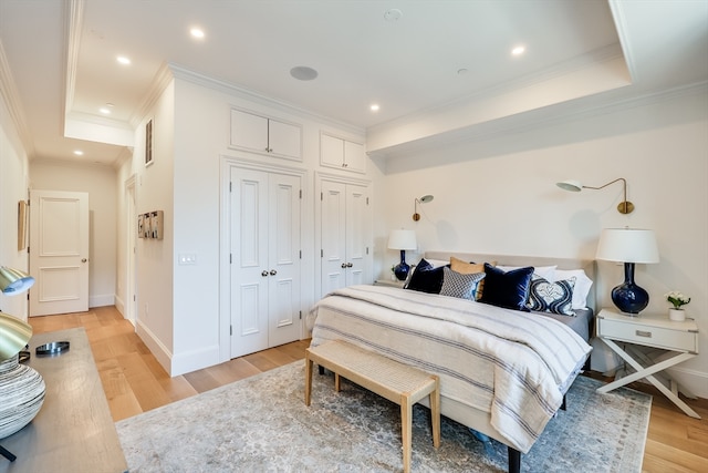 bedroom with a tray ceiling, ornamental molding, a closet, and light wood-type flooring