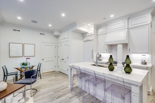 kitchen featuring white cabinetry, a center island with sink, light hardwood / wood-style flooring, ornamental molding, and a kitchen breakfast bar