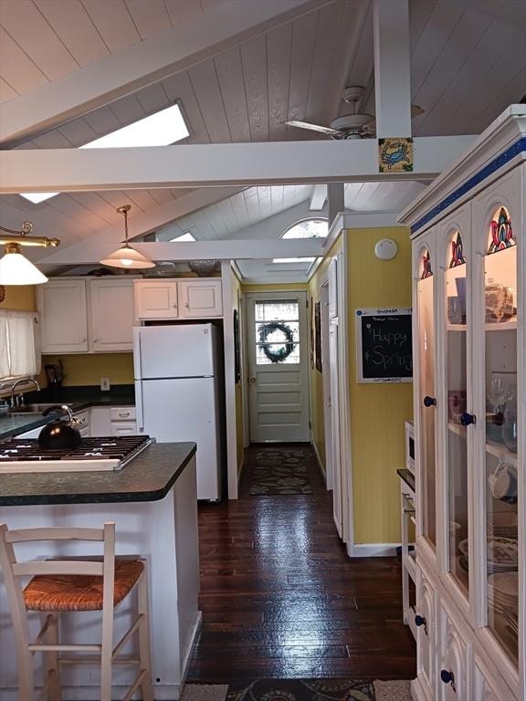 kitchen with dark countertops, vaulted ceiling with beams, freestanding refrigerator, white cabinetry, and dark wood-style flooring