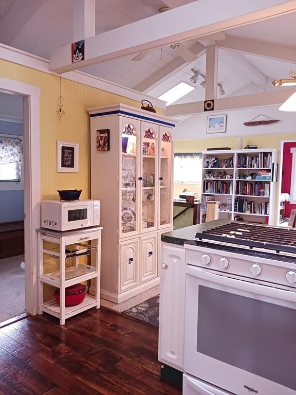kitchen with lofted ceiling with beams, dark countertops, dark wood finished floors, white cabinetry, and white appliances