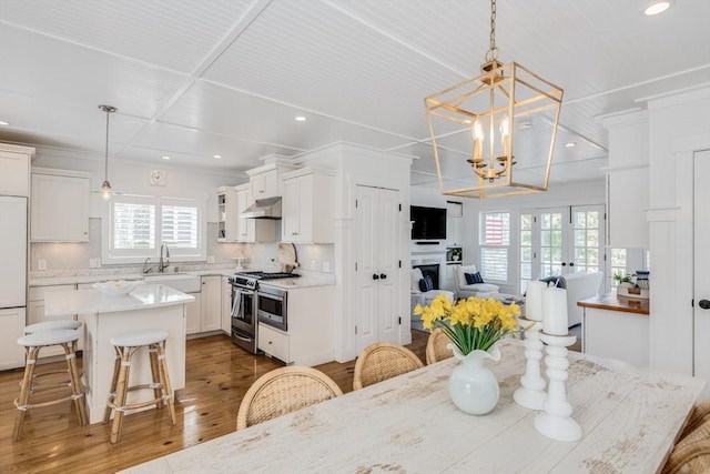 dining room featuring wood finished floors, recessed lighting, a fireplace, crown molding, and a chandelier