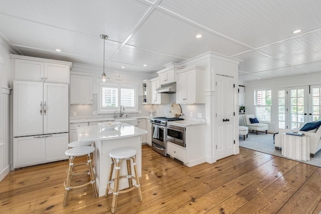 kitchen with gas stove, light wood-type flooring, under cabinet range hood, a kitchen breakfast bar, and open floor plan