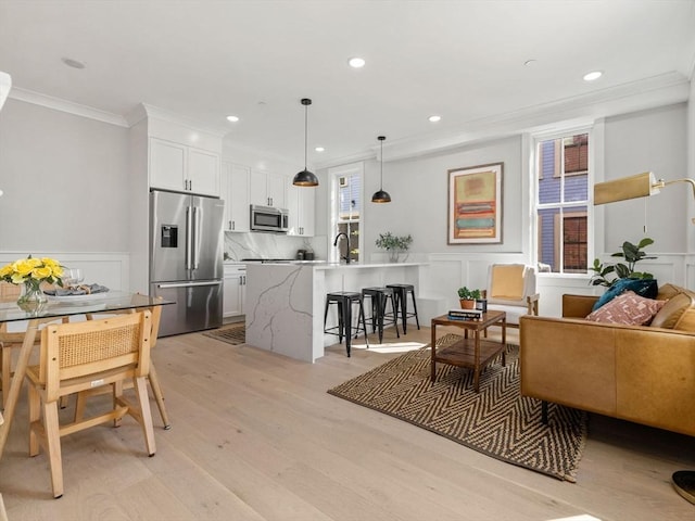 kitchen featuring white cabinets, crown molding, appliances with stainless steel finishes, decorative light fixtures, and a kitchen bar