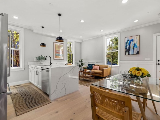 kitchen with white cabinetry, light hardwood / wood-style flooring, crown molding, pendant lighting, and appliances with stainless steel finishes