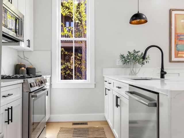 interior space featuring sink, white cabinetry, stainless steel appliances, and hanging light fixtures