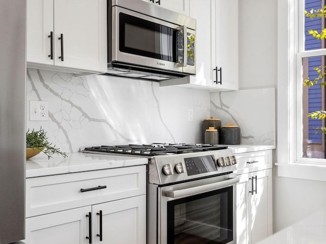 kitchen featuring white cabinets, appliances with stainless steel finishes, backsplash, and light stone countertops