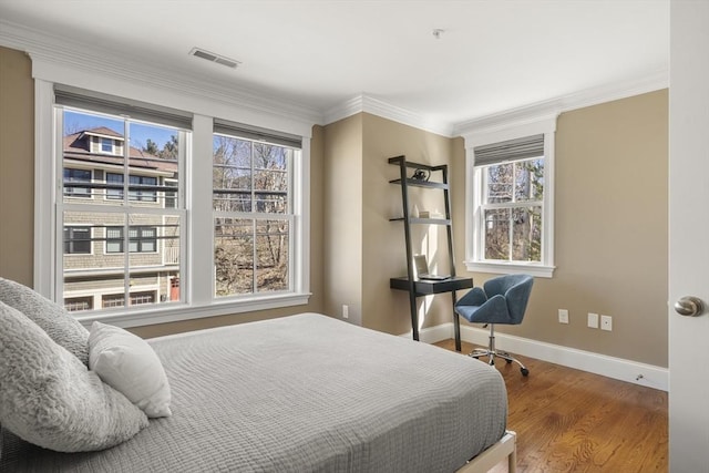 bedroom with ornamental molding, wood finished floors, visible vents, and baseboards