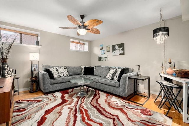 living area featuring ceiling fan with notable chandelier, baseboards, and wood finished floors