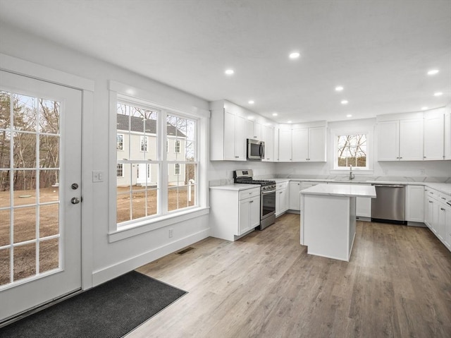 kitchen with white cabinetry, a center island, stainless steel appliances, and light hardwood / wood-style floors