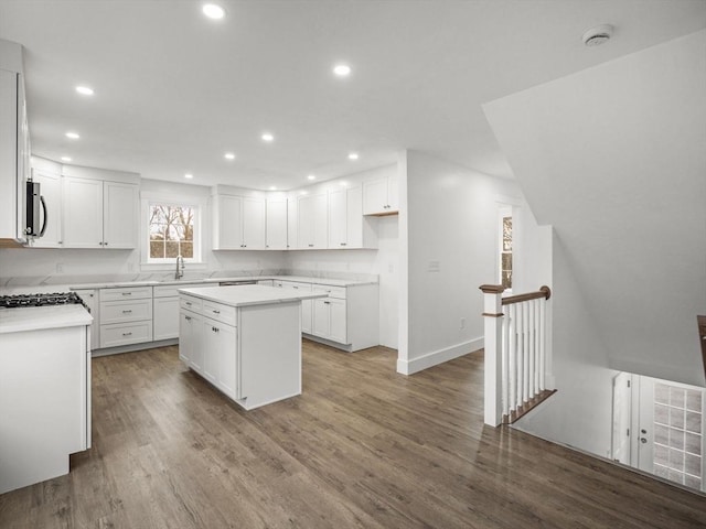 kitchen with hardwood / wood-style floors, a kitchen island, white cabinetry, and sink