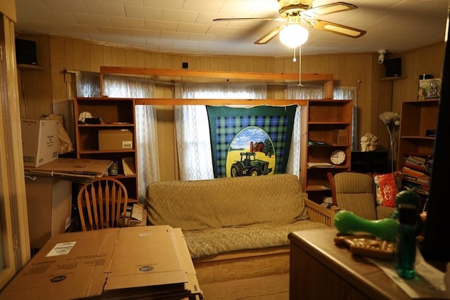 sitting room featuring ceiling fan and wooden walls