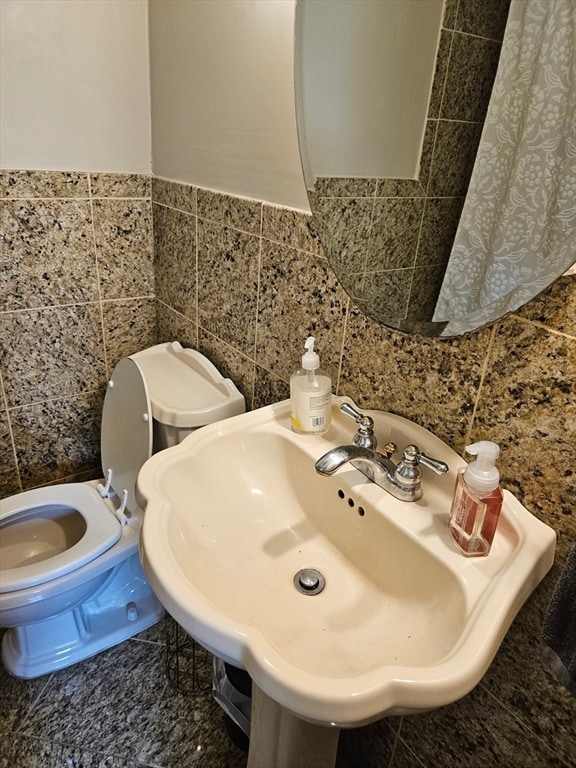 bathroom featuring toilet, tile walls, and sink