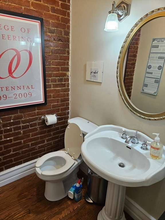 bathroom featuring toilet, hardwood / wood-style floors, and brick wall