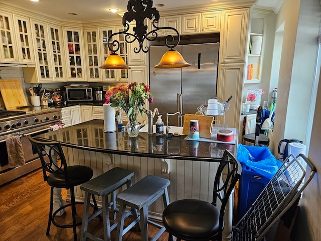 kitchen featuring high quality appliances, hanging light fixtures, a kitchen bar, and dark hardwood / wood-style flooring