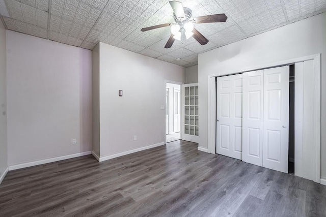 unfurnished bedroom featuring ceiling fan, baseboards, wood finished floors, a closet, and an ornate ceiling