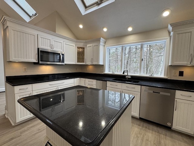 kitchen featuring a kitchen island, appliances with stainless steel finishes, vaulted ceiling with skylight, white cabinetry, and sink