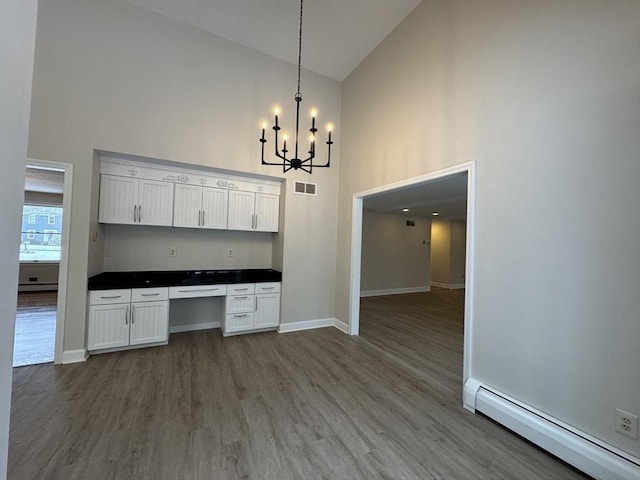 kitchen featuring built in desk, high vaulted ceiling, decorative light fixtures, white cabinetry, and a baseboard heating unit