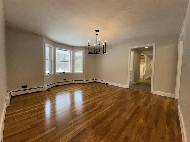 unfurnished dining area with an inviting chandelier, baseboard heating, and hardwood / wood-style floors