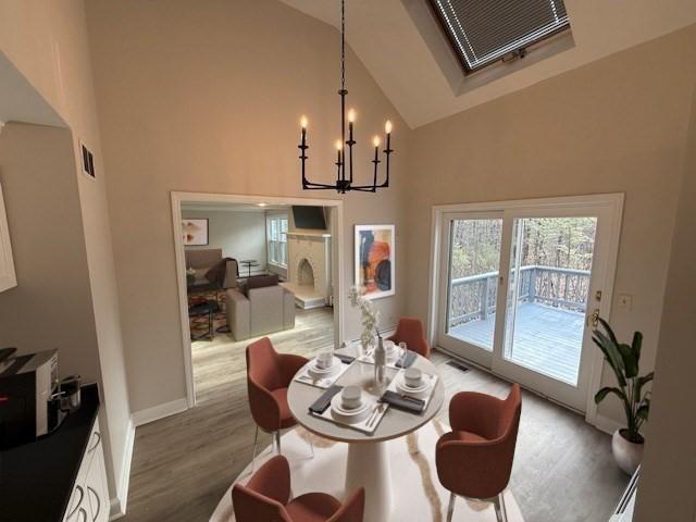 dining room with hardwood / wood-style floors, a notable chandelier, high vaulted ceiling, and a skylight