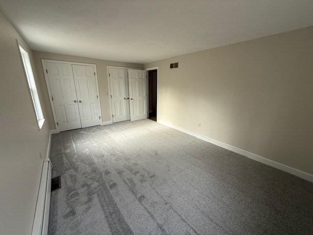 unfurnished bedroom with a baseboard heating unit, two closets, and carpet flooring