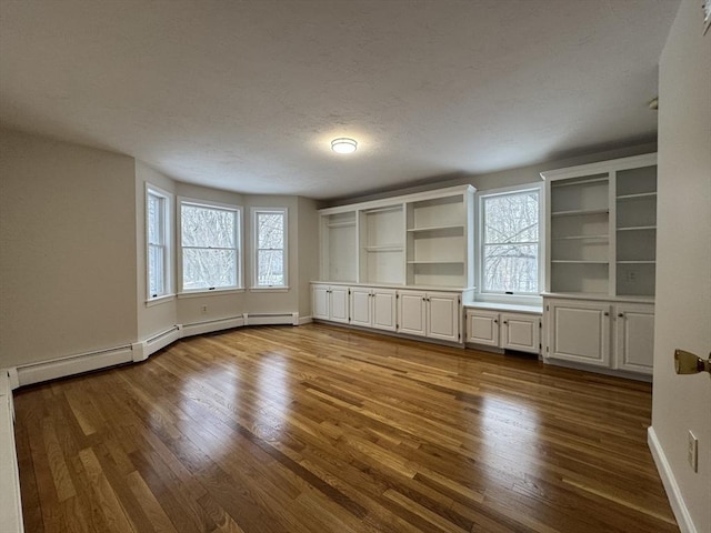 unfurnished living room with a baseboard heating unit and light hardwood / wood-style floors