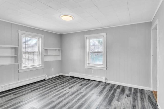 empty room with ornamental molding, hardwood / wood-style floors, built in features, and a baseboard radiator