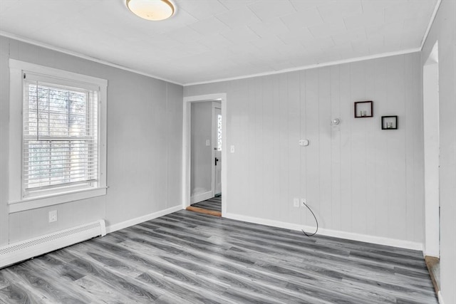 unfurnished room featuring baseboard heating, ornamental molding, and hardwood / wood-style floors