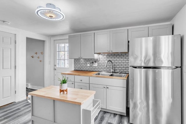 kitchen featuring butcher block counters, sink, light hardwood / wood-style flooring, decorative backsplash, and stainless steel refrigerator