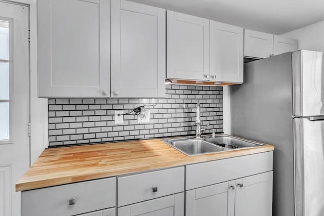 kitchen with a wealth of natural light, butcher block counters, backsplash, white cabinetry, and sink