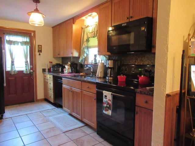 kitchen with dark stone countertops, black appliances, light tile patterned floors, pendant lighting, and sink