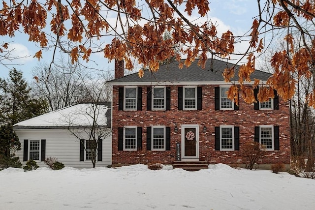 colonial house featuring a chimney and brick siding