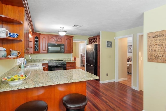 kitchen with light stone counters, visible vents, dark wood-type flooring, a peninsula, and black appliances