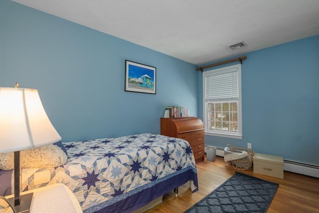 bedroom featuring a baseboard radiator, visible vents, and wood finished floors