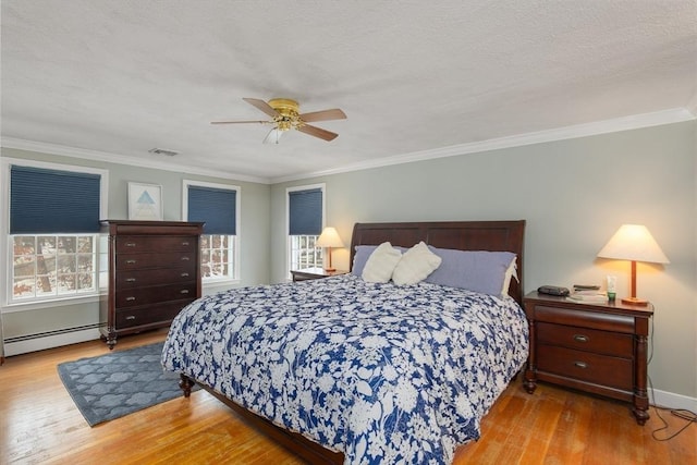 bedroom with a ceiling fan, crown molding, a baseboard heating unit, and wood finished floors