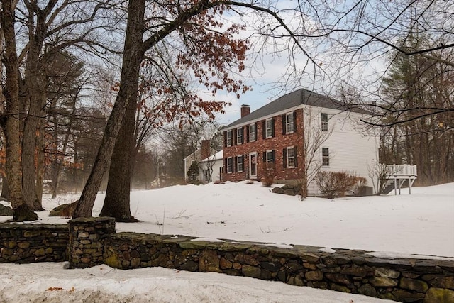 view of snowy exterior with brick siding and a chimney