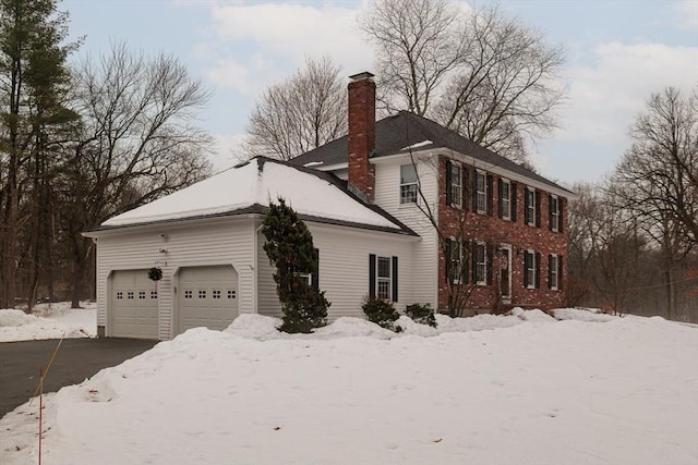 view of snow covered exterior featuring a garage, a chimney, and aphalt driveway