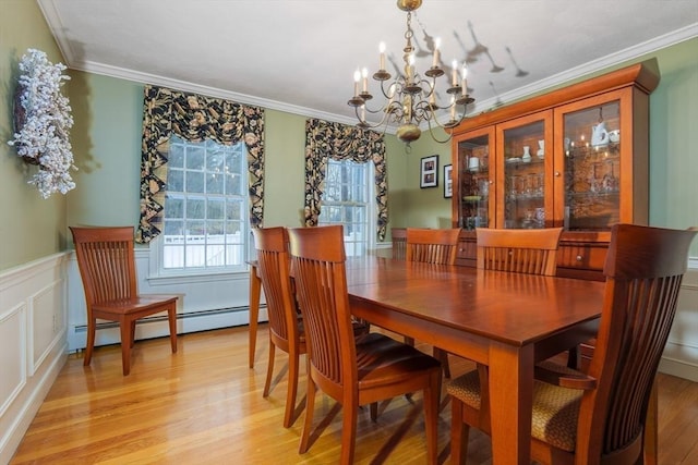 dining space featuring a notable chandelier, light wood-style floors, baseboard heating, wainscoting, and crown molding