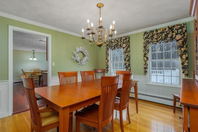 dining area with a wainscoted wall, light wood-style flooring, ornamental molding, a baseboard heating unit, and a notable chandelier