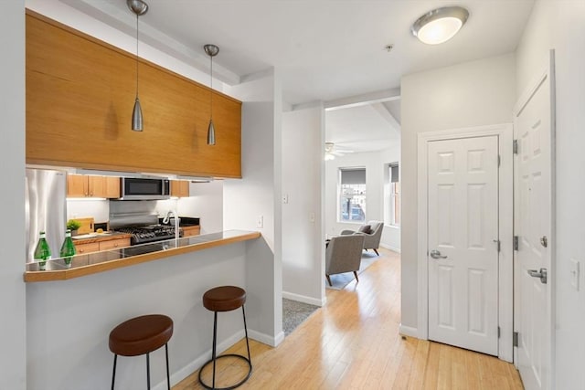 kitchen featuring pendant lighting, a kitchen breakfast bar, ceiling fan, stainless steel appliances, and light wood-type flooring