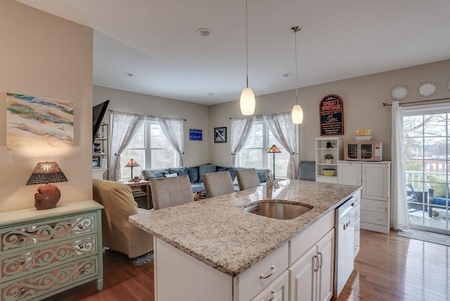 kitchen featuring a center island with sink, white cabinets, sink, light stone countertops, and decorative light fixtures