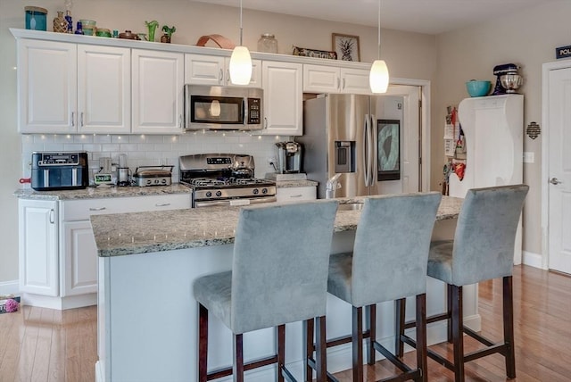 kitchen featuring tasteful backsplash, hanging light fixtures, white cabinets, and stainless steel appliances