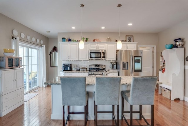 kitchen with light stone countertops, stainless steel appliances, white cabinets, hanging light fixtures, and an island with sink