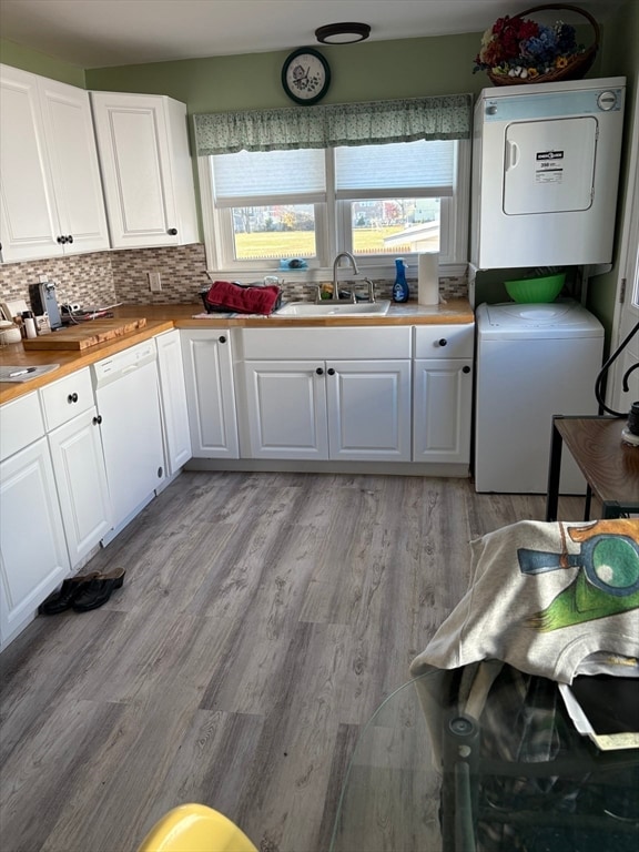 kitchen with sink, stacked washing maching and dryer, backsplash, white cabinets, and light wood-type flooring