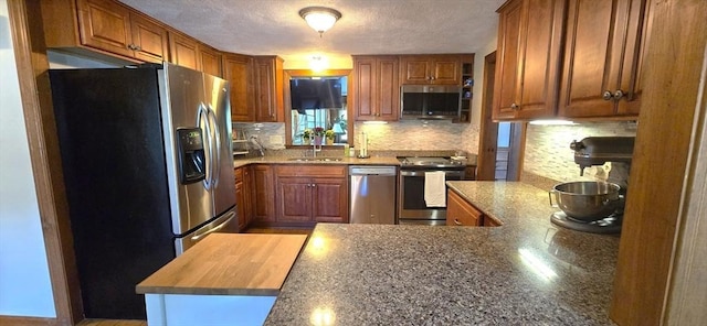 kitchen with appliances with stainless steel finishes, brown cabinets, tasteful backsplash, a peninsula, and a textured ceiling