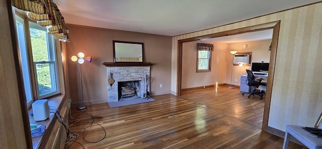 unfurnished living room featuring wood finished floors, an office area, a brick fireplace, baseboards, and a wall mounted air conditioner