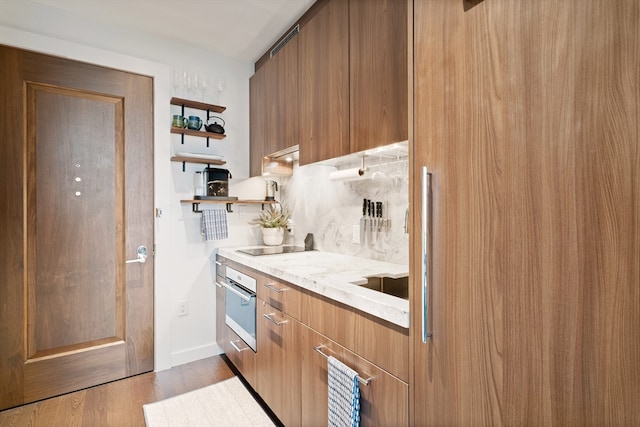 kitchen with hardwood / wood-style flooring, black electric stovetop, oven, and tasteful backsplash