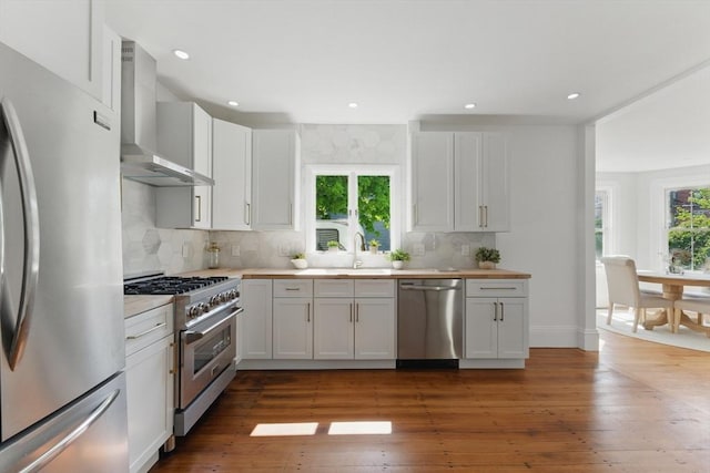 kitchen featuring stainless steel appliances, wall chimney exhaust hood, light countertops, a sink, and decorative backsplash