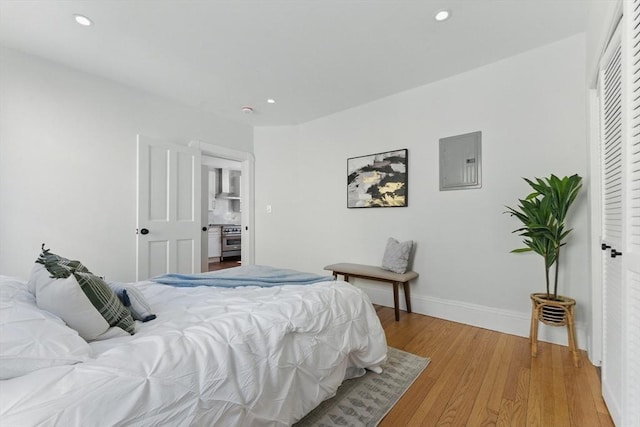 bedroom featuring electric panel, light wood-style floors, recessed lighting, baseboards, and a closet