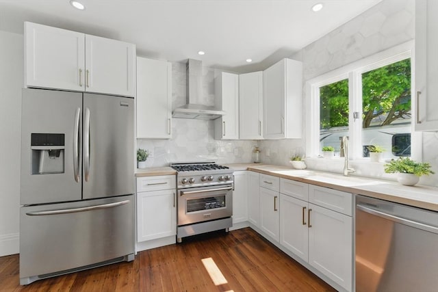 kitchen featuring stainless steel appliances, wall chimney exhaust hood, a sink, white cabinetry, and light countertops