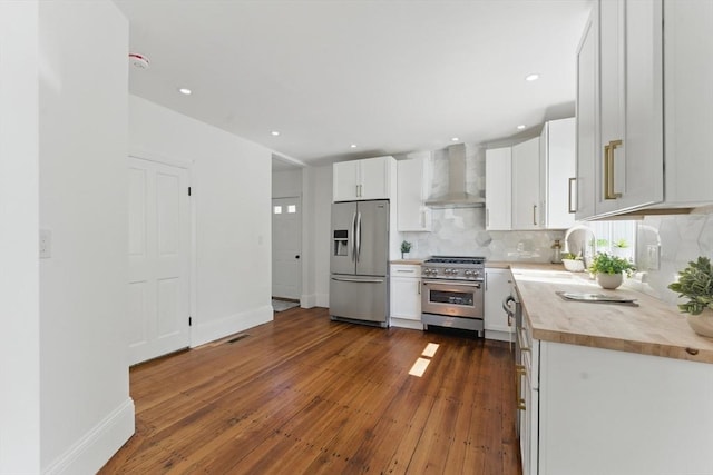 kitchen featuring appliances with stainless steel finishes, wall chimney range hood, tasteful backsplash, dark wood-style flooring, and white cabinetry